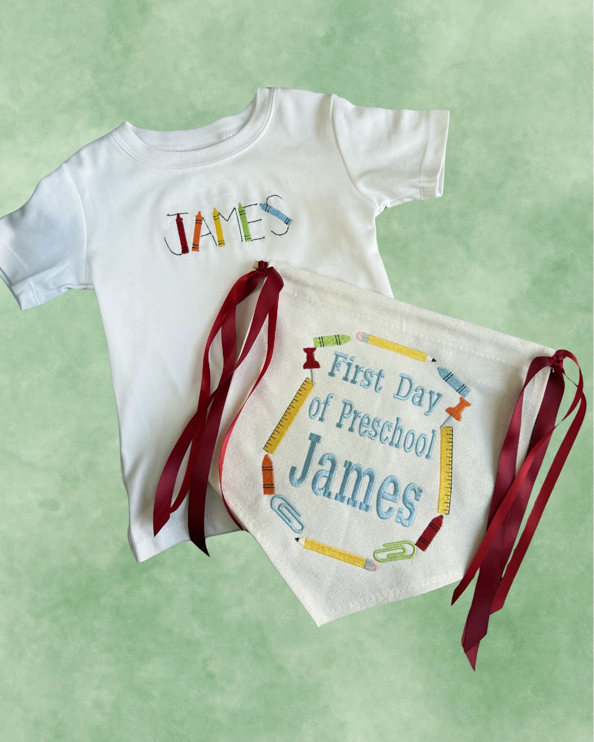 Personalized white tee with a name embroidered in crayon letters, shown with a matching first-day-of-school banner
